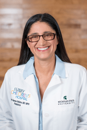 Dr. Mona Hanna Dr. Mona Hanna in her medical coat wearing classes smiling.