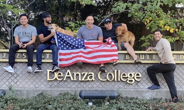 five student veterans with dog and flag, sitting on wall
